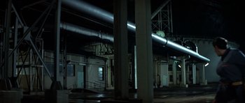 Movie still from “The Living Daylights” (1987), directed by John Glen – A clock on the side of a building in the dark; Extreme Wide shot, High angle