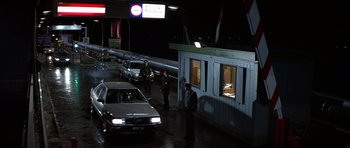 Movie still from “The Living Daylights” (1987), directed by John Glen – A group of men standing in front of a building at night; Wide shot, High angle