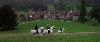 Movie still from “The Living Daylights” (1987), directed by John Glen – Three people riding horses in a field near a building; Extreme Wide shot, High angle