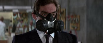 Movie still from “The Living Daylights” (1987), directed by John Glen – A man in a suit and tie wearing a gas mask; Close Up shot, Low angle