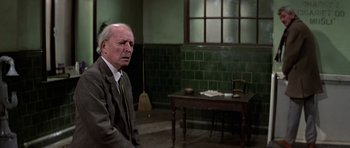 Movie still from “The Living Daylights” (1987), directed by John Glen – An older man in a suit sitting in front of a table; Medium shot, Over the shoulder angle