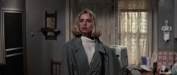 Movie still from “The Living Daylights” (1987), directed by John Glen – A woman in a trench coat standing in a room; Close Up shot, Low angle