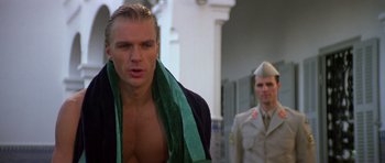 Movie still from “The Living Daylights” (1987), directed by John Glen – A man with a towel around his neck standing next to a man in a uniform; Close Up shot, Low angle