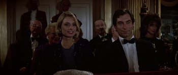 Movie still from “The Living Daylights” (1987), directed by John Glen – A man and a woman are sitting in front of other people; Medium shot, Low angle
