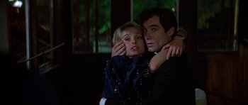 Movie still from “The Living Daylights” (1987), directed by John Glen – A man and a woman hugging each other in front of a window; Close Up shot, Low angle