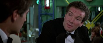 Movie still from “The Living Daylights” (1987), directed by John Glen – A man in a tuxedo sitting at a table in a restaurant; Close Up shot, Over the shoulder angle