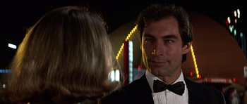 Movie still from “The Living Daylights” (1987), directed by John Glen – A man in a tuxedo talking to a woman in front of lights; Close Up shot, Low angle