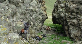 Movie still from “The Loneliest Planet” (2011), directed by Julia Loktev – A man climbing up a rock wall while another man sits on the ground next to him; Wide shot, Low angle
