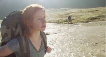 Movie still from “The Loneliest Planet” (2011), directed by Julia Loktev – A woman with a backpack standing in shallow water with a man walking in the background; Medium shot, Low angle