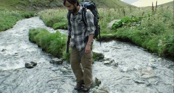 Movie still from “The Loneliest Planet” (2011), directed by Julia Loktev – A man standing in a river with a backpack; Medium shot, High angle