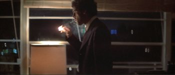 Movie still from “The Long Goodbye” (1973), directed by Robert Altman – A man in a suit smoking a cigarette in a dark room; Medium shot, Low angle