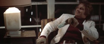 Movie still from “The Long Goodbye” (1973), directed by Robert Altman – A person sitting in a chair holding a dollar bill; Medium shot, Low angle