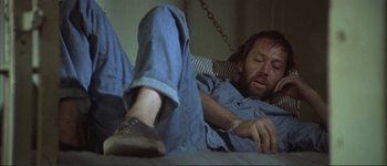 Movie still from “The Long Goodbye” (1973), directed by Robert Altman – A man laying in bed with his feet up on the ground; Medium shot, High angle