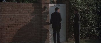 Movie still from “The Long Goodbye” (1973), directed by Robert Altman – A man standing in front of a white door; Wide shot, High angle