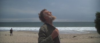 Movie still from “The Long Goodbye” (1973), directed by Robert Altman – An older man with a beard is standing on the beach; Medium shot, Low angle