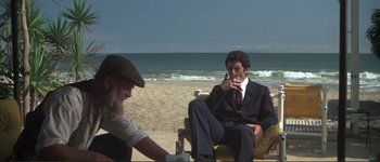 Movie still from “The Long Goodbye” (1973), directed by Robert Altman – A man sitting on a chair next to a man on the beach; Wide shot, High angle