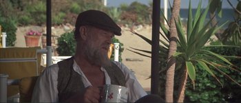 Movie still from “The Long Goodbye” (1973), directed by Robert Altman – An old man with a beard and a hat holding a mug; Medium shot, Over the shoulder angle