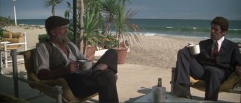 Movie still from “The Long Goodbye” (1973), directed by Robert Altman – A man sitting on a chair next to a bottle of beer; Wide shot, Low angle