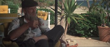 Movie still from “The Long Goodbye” (1973), directed by Robert Altman – An old man sitting on a chair drinking a cup of coffee; Medium shot, High angle