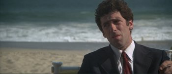 Movie still from “The Long Goodbye” (1973), directed by Robert Altman – A man in a suit sitting on a bench by the beach; Close Up shot, Low angle