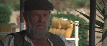 Movie still from “The Long Goodbye” (1973), directed by Robert Altman – An old man with a beard and a hat is sitting outside; Close Up shot, Over the shoulder angle