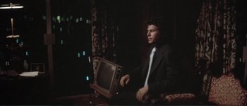 Movie still from “The Long Goodbye” (1973), directed by Robert Altman – A man in a suit and tie sitting in front of a television; Medium shot, Low angle