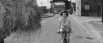 Movie still from “The Longest Day” (1962), directed by Ken Annakin – A black and white photo of a woman riding a bike; Medium shot, Low angle