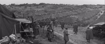 Movie still from “The Longest Day” (1962), directed by Ken Annakin – A black and white photo of a group of men standing around tents; Extreme Wide shot, High angle
