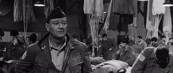 Movie still from “The Longest Day” (1962), directed by Ken Annakin – An older man wearing a military uniform in a room full of people; Medium shot, Over the shoulder angle
