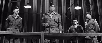 Movie still from “The Longest Day” (1962), directed by Ken Annakin – A man in a military uniform standing next to a wooden fence; Medium shot, Low angle