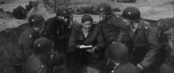 Movie still from “The Longest Day” (1962), directed by Ken Annakin – A group of men sitting on the ground with a book; Medium shot, High angle