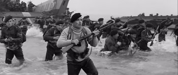 Movie still from “The Longest Day” (1962), directed by Ken Annakin – A man holding a gun while standing in the water; Medium shot, Low angle