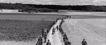 Movie still from “The Longest Day” (1962), directed by Ken Annakin – A black and white photo of a group of soldiers on a dirt road; Extreme Wide shot, High angle