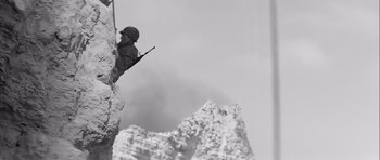 Movie still from “The Longest Day” (1962), directed by Ken Annakin – A man holding a rifle while standing on top of a mountain; Medium shot, Low angle
