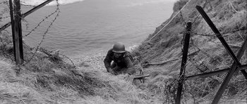 Movie still from “The Longest Day” (1962), directed by Ken Annakin – A man in a military uniform climbing a hill; Medium shot, High angle