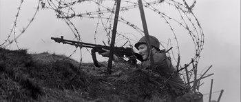 Movie still from “The Longest Day” (1962), directed by Ken Annakin – A man with a rifle in a field with barbed wire; Medium shot, Low angle
