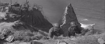 Movie still from “The Longest Day” (1962), directed by Ken Annakin – Two men in military uniforms laying on the ground; Wide shot, High angle