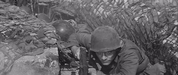 Movie still from “The Longest Day” (1962), directed by Ken Annakin – Two men in military uniforms are laying on the ground; Medium shot, Low angle