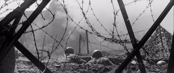 Movie still from “The Longest Day” (1962), directed by Ken Annakin – Two soldiers are laying in a field with barbed wire; Wide shot, Low angle