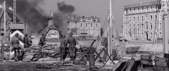 Movie still from “The Longest Day” (1962), directed by Ken Annakin – Two men standing in front of a building with smoke billowing out of it; Extreme Wide shot, High angle