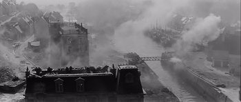 Movie still from “The Longest Day” (1962), directed by Ken Annakin – A black and white photo of a city with smoke coming out of it; Extreme Wide shot, High angle
