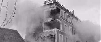 Movie still from “The Longest Day” (1962), directed by Ken Annakin – Smoke billows out of a building that has been destroyed; Wide shot, Low angle