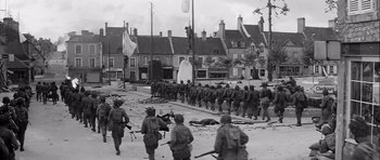 Movie still from “The Longest Day” (1962), directed by Ken Annakin – A black and white photo of soldiers marching down a street; Extreme Wide shot, High angle