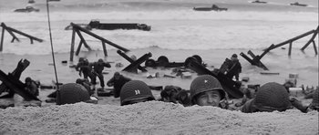 Movie still from “The Longest Day” (1962), directed by Ken Annakin – A group of men in helmets on a beach; Medium shot, High angle