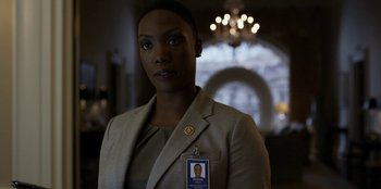 Movie still from “House of Cards” (2013), created by Beau Willimon – A woman in a tan jacket with a name tag on her chest; Close Up shot, Low angle