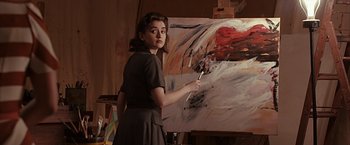 Movie still from “The Longest Ride” (2015), directed by George Tillman Jr. – A woman holding a paintbrush in front of a painting; Medium shot, Over the shoulder angle