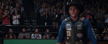 Movie still from “The Longest Ride” (2015), directed by George Tillman Jr. – A man wearing a cowboy hat and a leather vest stands in front of an audience; Close Up shot, Over the shoulder angle