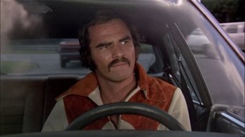 Movie still from “The Longest Yard” (1974), directed by Robert Aldrich – A man sitting in the drivers seat of a car; Close Up shot, Over the shoulder angle