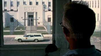 Movie still from “The Longest Yard” (1974), directed by Robert Aldrich – An older man looking out of a window at a white van; Extreme Wide shot, Over the shoulder angle