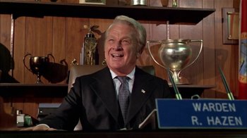 Movie still from “The Longest Yard” (1974), directed by Robert Aldrich – An older man sitting at a desk in front of a trophy; Close Up shot, Low angle